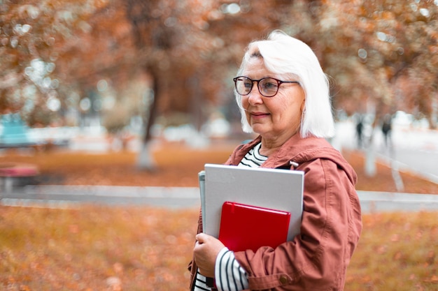 Volwassen vrouw student met boeken en tijdschriften in haar handen staat in het park