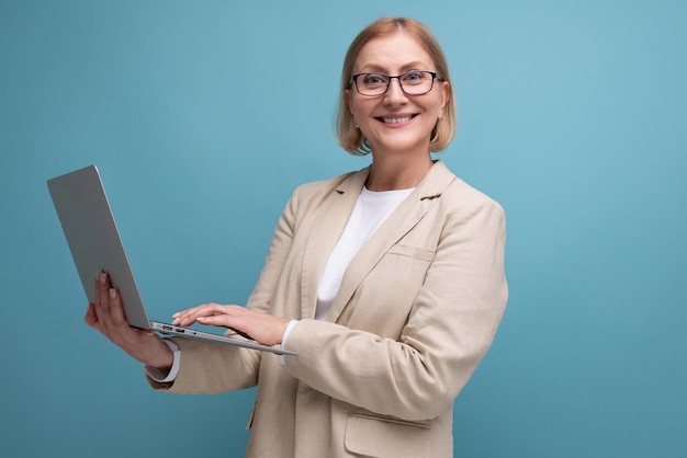 Volwassen vrouw van middelbare leeftijd in jas beheerst nieuwe techniek met behulp van laptop op studioachtergrond met kopie