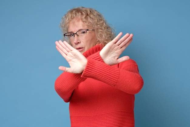 Foto volwassen vrouw van middelbare leeftijd met een rode trui en een bril die een stopgebaar doet