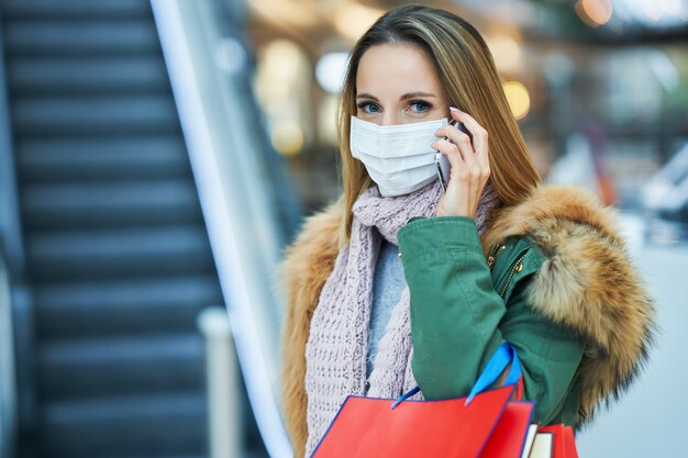 volwassen vrouw winkelen in winkelcentrum met smartphone met een masker, coronavirusconcept