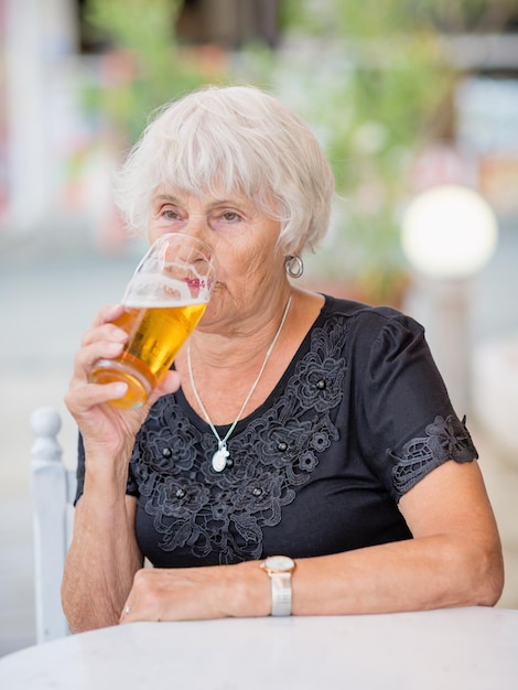 Volwassen vrouw zit aan een tafel in een zomercafé en drinkt bier