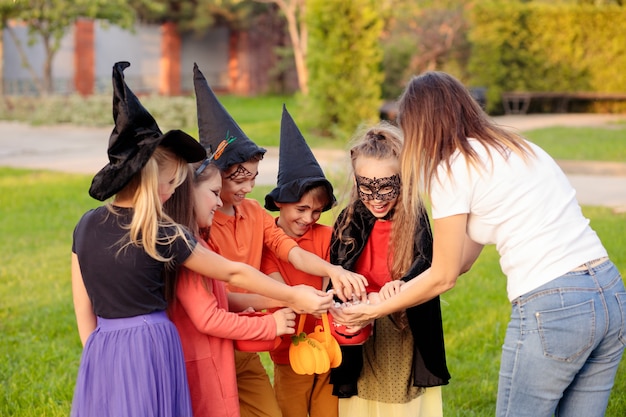 Volwassen vrouwtje snoep te geven aan gelukkige kinderen in kostuums van Halloween tijdens trick or treat-evenement in park