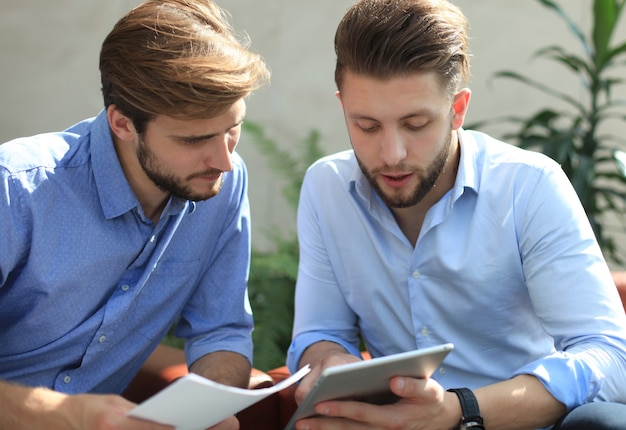 Volwassen zakenman die een digitale tablet gebruikt om informatie te bespreken met een jongere collega in een modern bedrijfskantoor