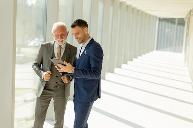 Volwassen zakenman en zijn jonge collega bespreken een financieel verslag op een digitale tablet in de kantoorcorridor