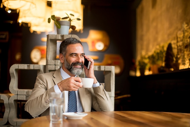 volwassen zakenman koffie drinken in café en het gebruik van mobiele telefoon