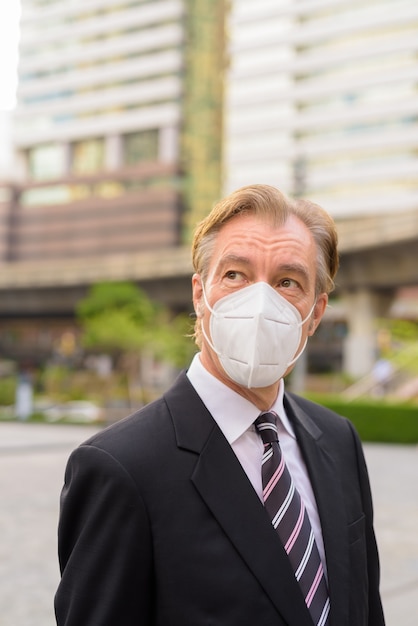 Foto volwassen zakenman met masker denken en kijken in de stad buiten