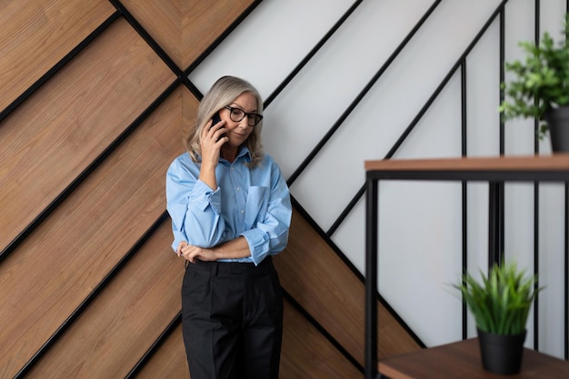 Volwassen zakenvrouw praten op een mobiele telefoon tegen de muur op kantoor met een succesvolle