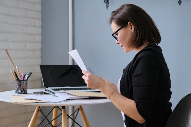 Volwassen zakenvrouw zittend aan een bureau in kantoor lezing papieren document