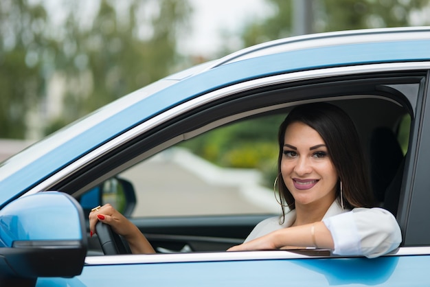 Volwassen zwartharige vrouwelijke chauffeur zit in blauwe auto te glimlachen