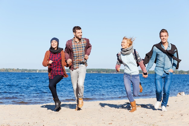 Voor altijd jong en vrij. Volledige lengte van twee mooie jonge stellen die samen langs het strand rennen en glimlachen