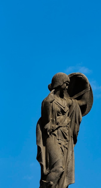 Voor een blauwe lucht staat een beeld van een vrouw met een schild erop.