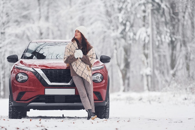 Voor haar auto Mooie jonge vrouw is buiten in de buurt van haar rode auto in de winter