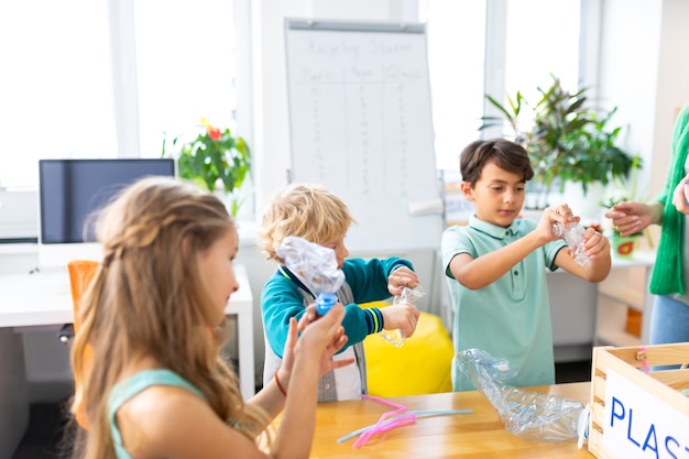 Voor toekomstige recycling. Schooljongens en hun mooie klasgenoot die plastic flessen vasthouden voor toekomstige recycling