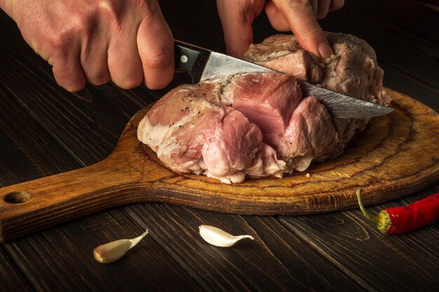 Voor vuur moet rauw vlees in kleine stukjes worden gesneden Handen van een chef-kok met een mes in de keuken