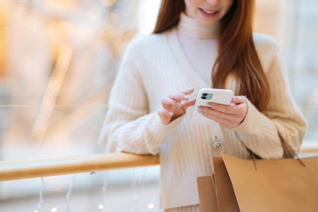 Vooraanzicht bijgesneden opname van onherkenbare jonge vrouw die een mobiele telefoon typt terwijl ze aan het winkelen is