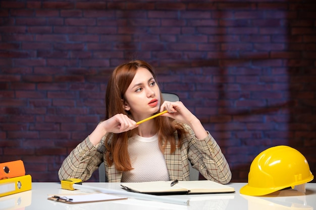 Foto vooraanzicht denkende vrouwelijke werknemer in bouwplaats zittend achter tafel agenda ingenieur zakelijk werkplan manager