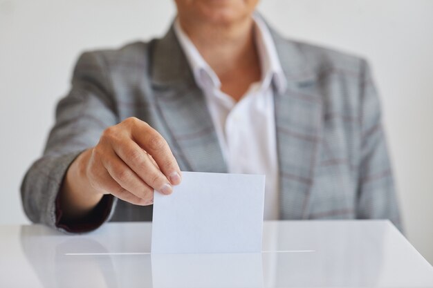 Vooraanzicht dichte omhooggaand van vrouwelijke hand die stembulletin in stembus zet tegen wit oppervlak op verkiezingsdag, exemplaarruimte