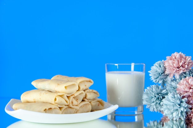 vooraanzicht gerolde zoete pannenkoeken met glas melk op een blauwe achtergrond maaltijd ontbijt eten ochtend suiker bloem kleur cake