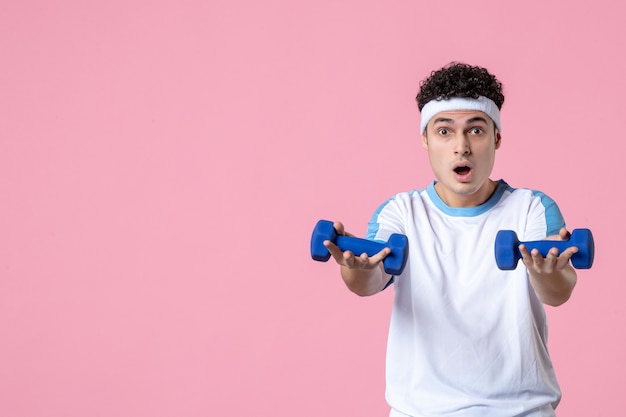 Vooraanzicht jong mannetje in sportkleren die met domoren op roze muur uitwerken