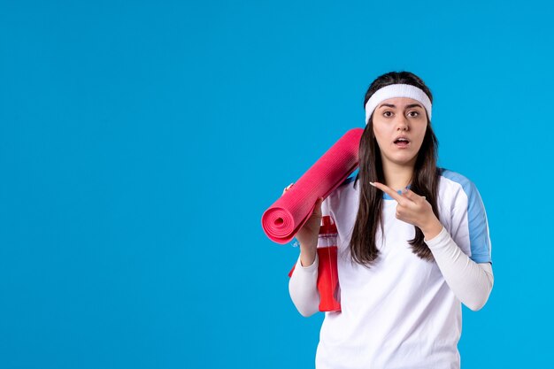 Vooraanzicht jong wijfje met yogamat op blauwe muur