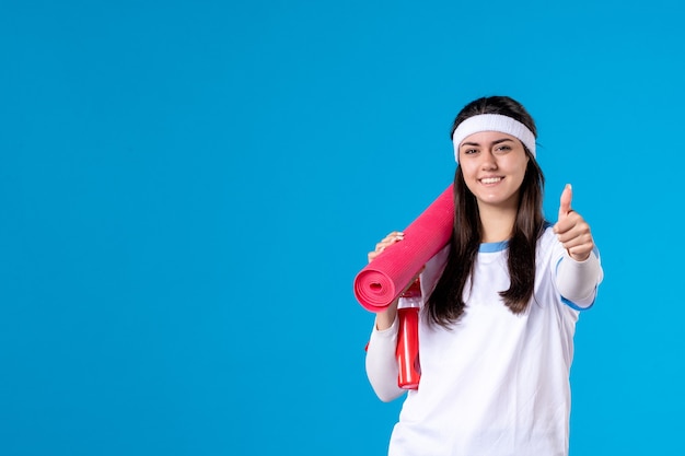 Vooraanzicht jong wijfje met yogamat op blauwe muur