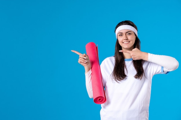 Vooraanzicht jong wijfje met yogamat op blauwe muur