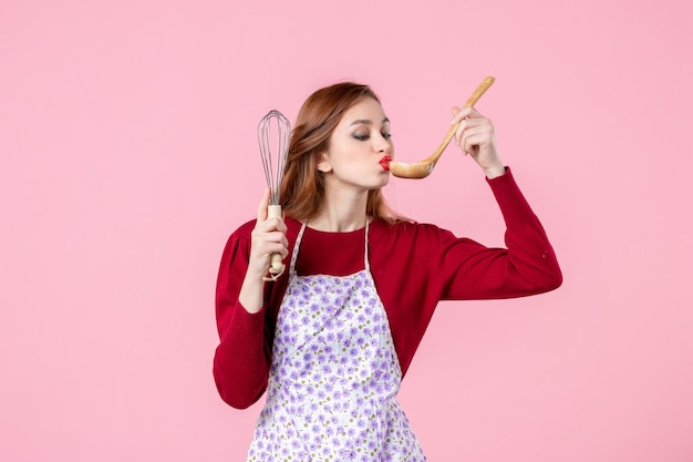 vooraanzicht jonge huisvrouw die garde vasthoudt en houten lepel proeft op roze achtergrond voedsel keuken taart vrouw winkelen geld keuken koken cake