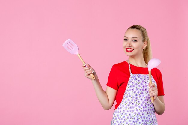 Vooraanzicht jonge huisvrouw met bestek op roze muur