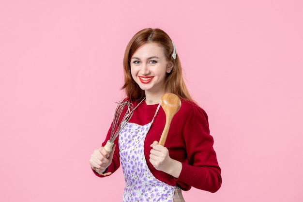 vooraanzicht jonge huisvrouw met garde en houten lepel op roze achtergrond koken deeg horizontale taart beroep vrouw cake keuken