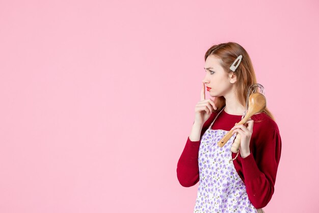 vooraanzicht jonge huisvrouw met lepel en garde opzij kijkend op roze achtergrond zoet eten cake taart keuken deeg keuken vrouw kleur