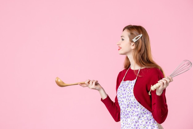 vooraanzicht jonge huisvrouw met lepel en garde opzij kijkend op roze achtergrond zoet eten taart keuken deeg koken keuken vrouw kleur