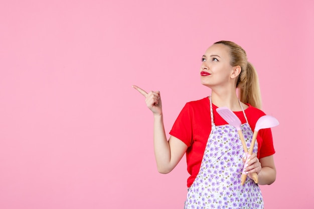 Vooraanzicht jonge huisvrouw poseren met bestek op roze muur