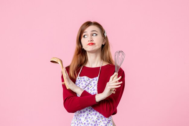 vooraanzicht jonge huisvrouw poseren met garde en houten lepel op roze achtergrond beroep koken deeg vrouw cake uniform horizontale taart