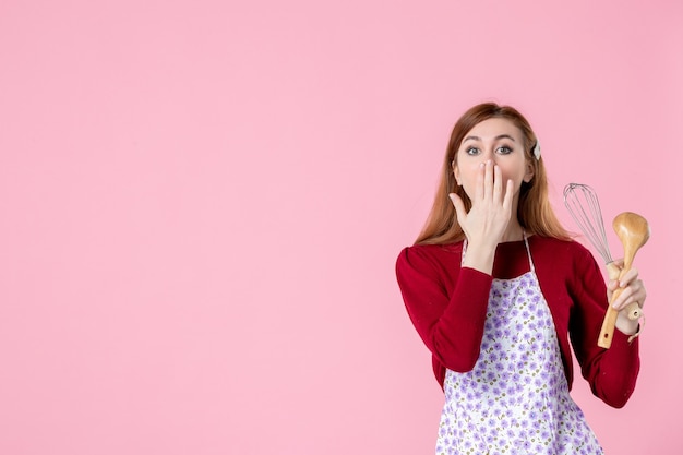 vooraanzicht jonge huisvrouw poseren met garde en houten lepel op roze achtergrond vrouw taart beroep uniform deeg horizontale keuken koken