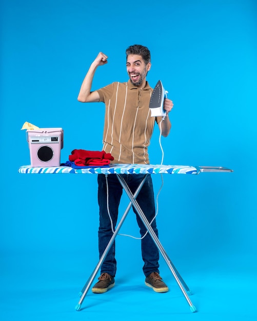 vooraanzicht jonge man achter strijkplank met ijzer vreugde op blauwe achtergrond kleur huishoudelijk werk wasserij wassen machine man emotie schoon