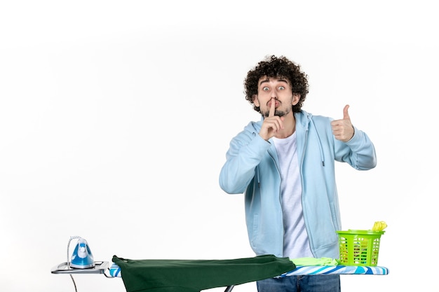 Foto vooraanzicht jonge man achter strijkplank op witte achtergrond huishoudelijk werk strijken wasgoed schoonmaken emotie man kleur mens