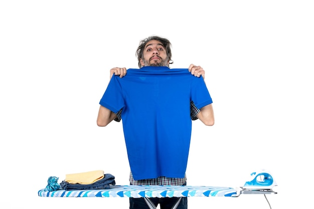 vooraanzicht jonge man achter strijkplank vouwen blauw shirt op witte achtergrond huishoudelijk werk werk ijzer wasserij man huis kleren schone machine