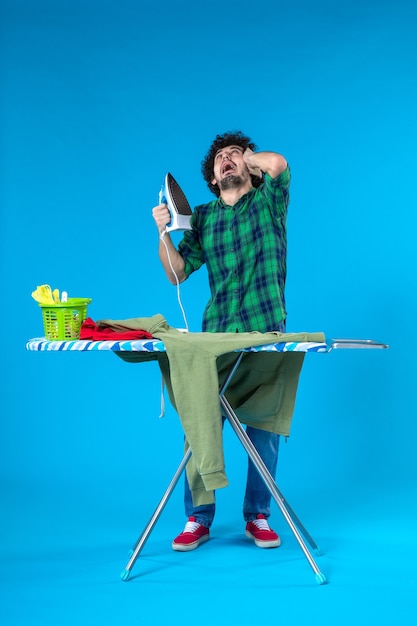 vooraanzicht jonge man bereidt zich voor om groene trui op blauwe achtergrond te strijken schone wasmachine huishoudelijk werk huiskleuren mens
