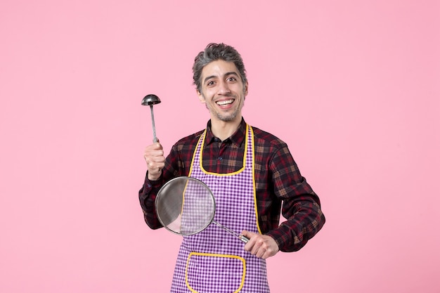 vooraanzicht jonge man in cape met zeef en lepel op roze achtergrond horizontaal voedsel keuken beroep uniform werknemer kok man keuken foto