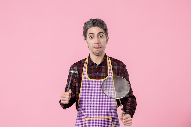 vooraanzicht jonge man in cape met zeef en lepel op roze achtergrond uniform keuken man keuken werknemer kok horizontaal