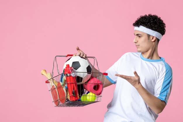 Vooraanzicht jonge man in sportkleding met mand vol met sport dingen roze muur