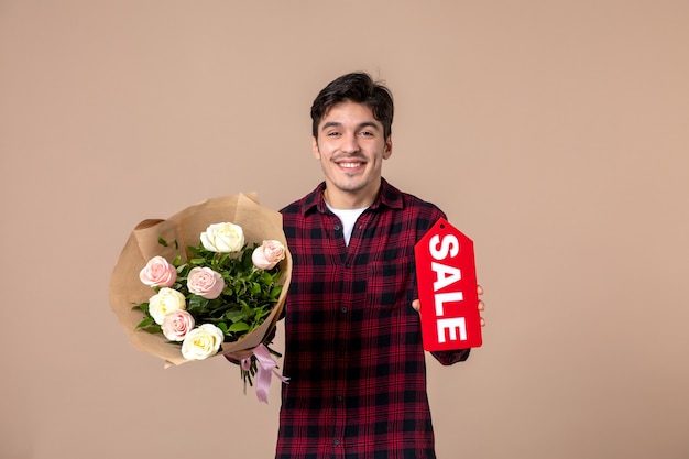 Vooraanzicht jonge man met mooie bloemen en verkoop naambordje op bruine muur