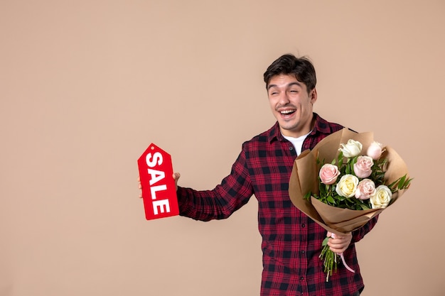 Vooraanzicht jonge man met mooie bloemen en verkoop naambordje op bruine muur