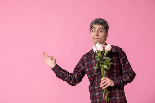Vooraanzicht jonge man met mooie roze rozen op roze muur
