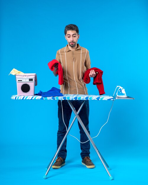 vooraanzicht jonge man met rode kleren achter strijkplank op de blauwe achtergrond kleur huishoudelijk werk wasserij man emotie schone wasmachine