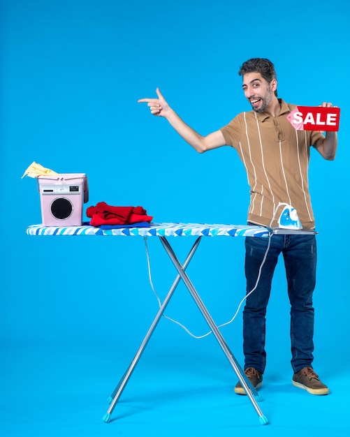 vooraanzicht jonge man met rode verkoop schrijven op blauwe achtergrond huishoudelijk werk winkelen huisvrouw wasmachine strijkijzer schone was