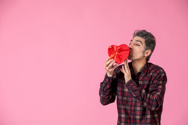 Vooraanzicht jonge man met rood hartvormig cadeau op roze muur