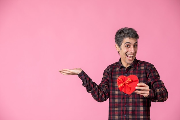 Vooraanzicht jonge man met rood hartvormig cadeau op roze muur