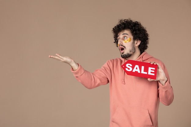 vooraanzicht jonge man met rood verkoopnaambordje op bruine achtergrond gezichtssalon huid winkelen therapie spa huidverzorging masseren foto