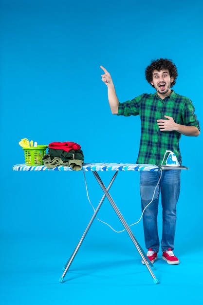 Foto vooraanzicht jonge man met strijkplank op blauwe achtergrond huis wasmachine schone menselijke kleren